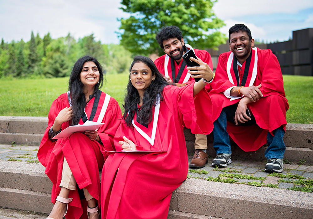 Students in graduation gowns taking a selfie outside