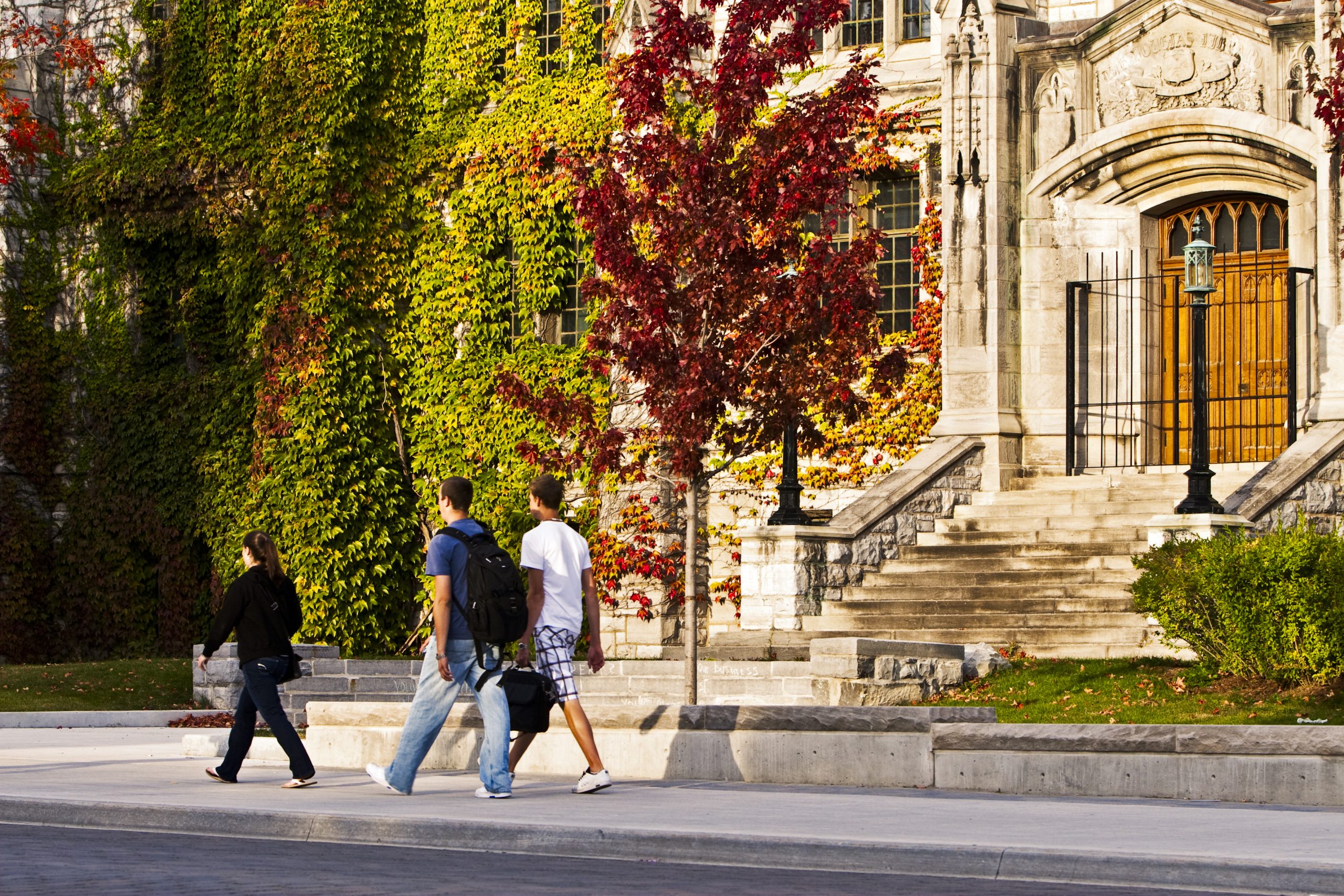 Photo of students walking to/from classes in front of a campus building in the fall.