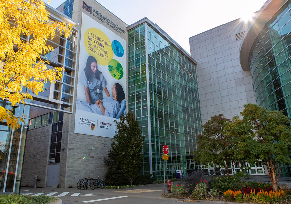 A picture of the outside of the Michael G. DeGroote Centre for Discovery and Learning at McMaster University in Hamilton, Ontario, Canada. The outside of the building features a garden and floor to ceiling glass windows.