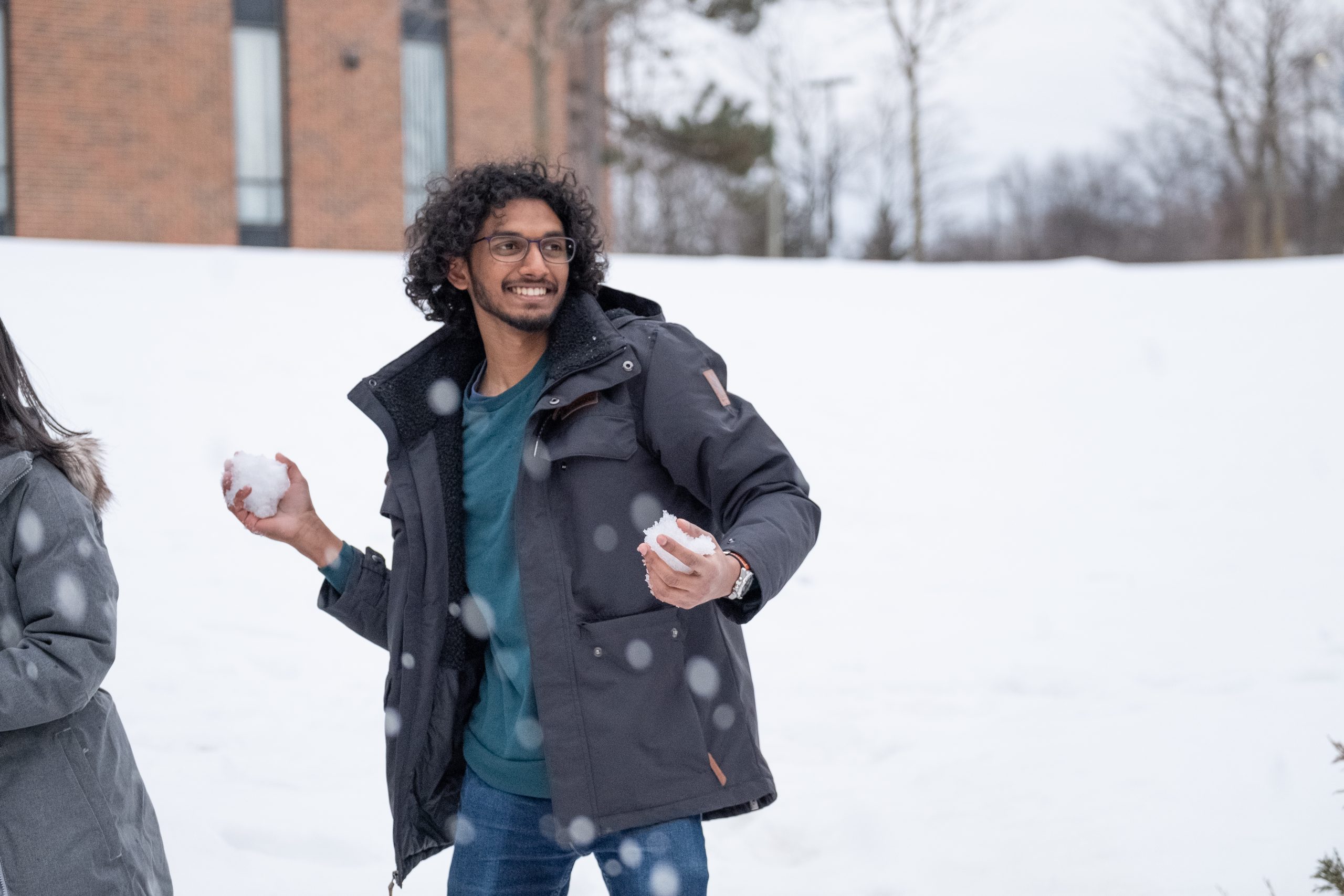 Man outside, participating in a snowball fight with a smile on face