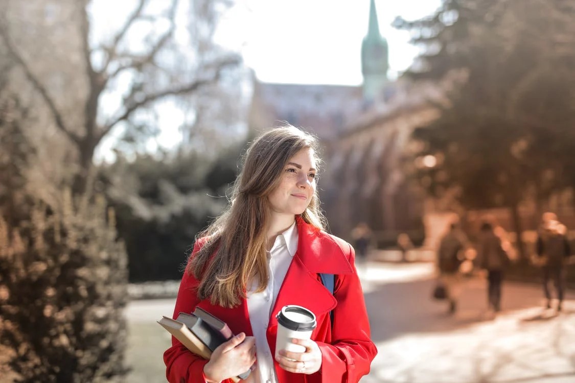 Female student in red jacket holding books and a coffee