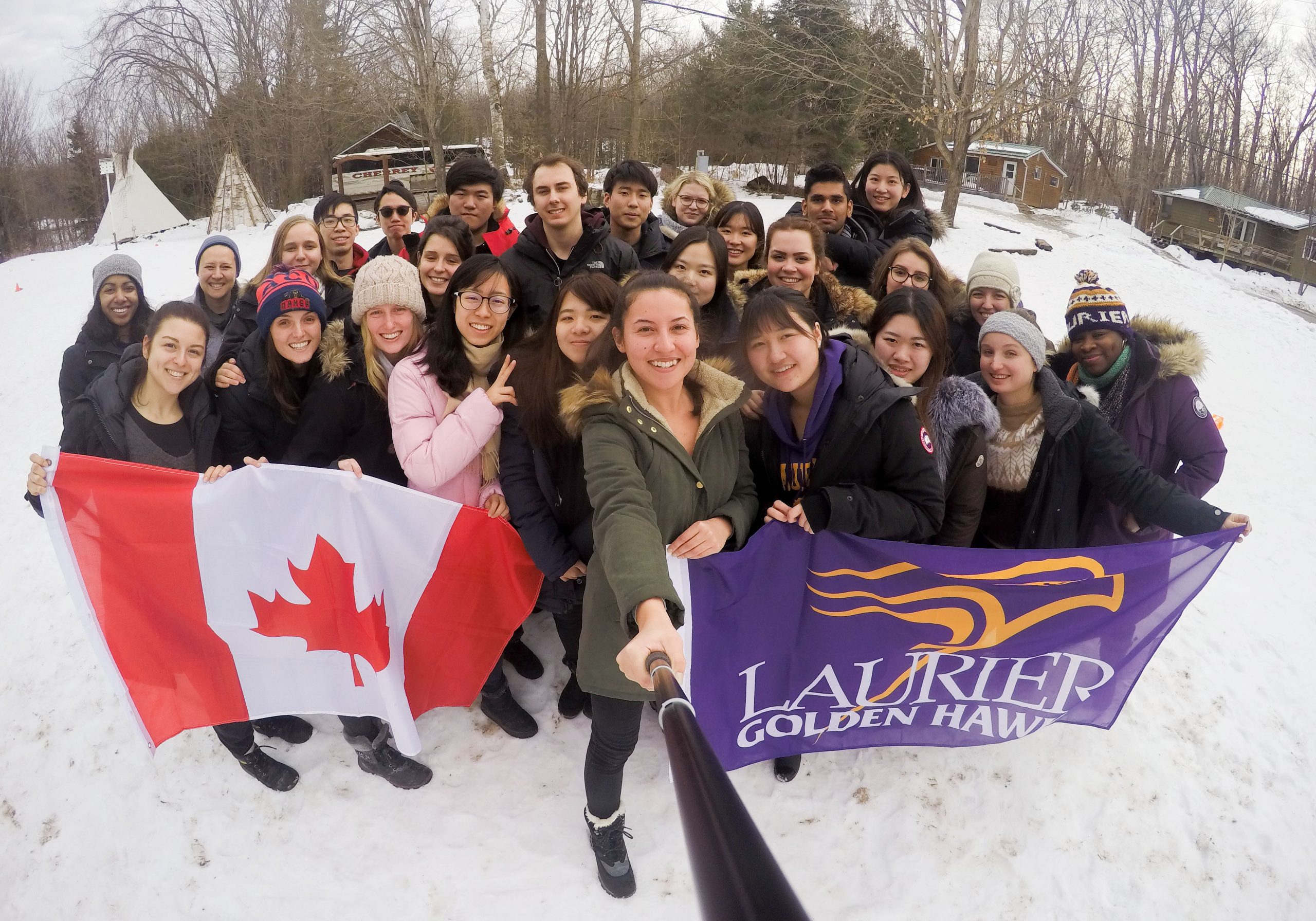 Students standing outside in the winter holding a Canadian flag and a Laurier flag