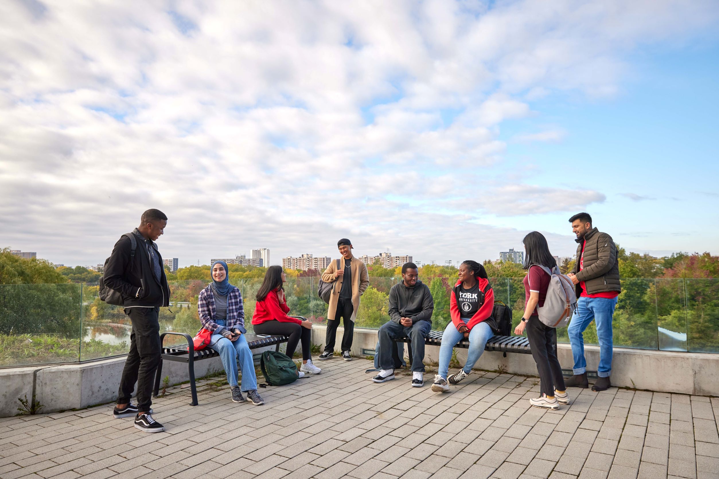 A group of eight students wearing backpacks gather on a terrace overlooking York University's Keele campus.