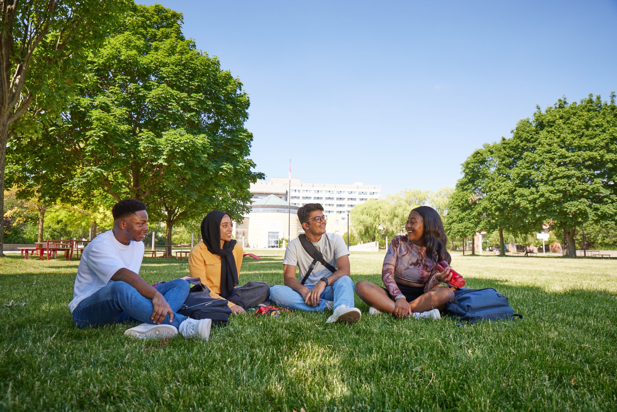 Four students sit together with backpacks in the grassy Commons